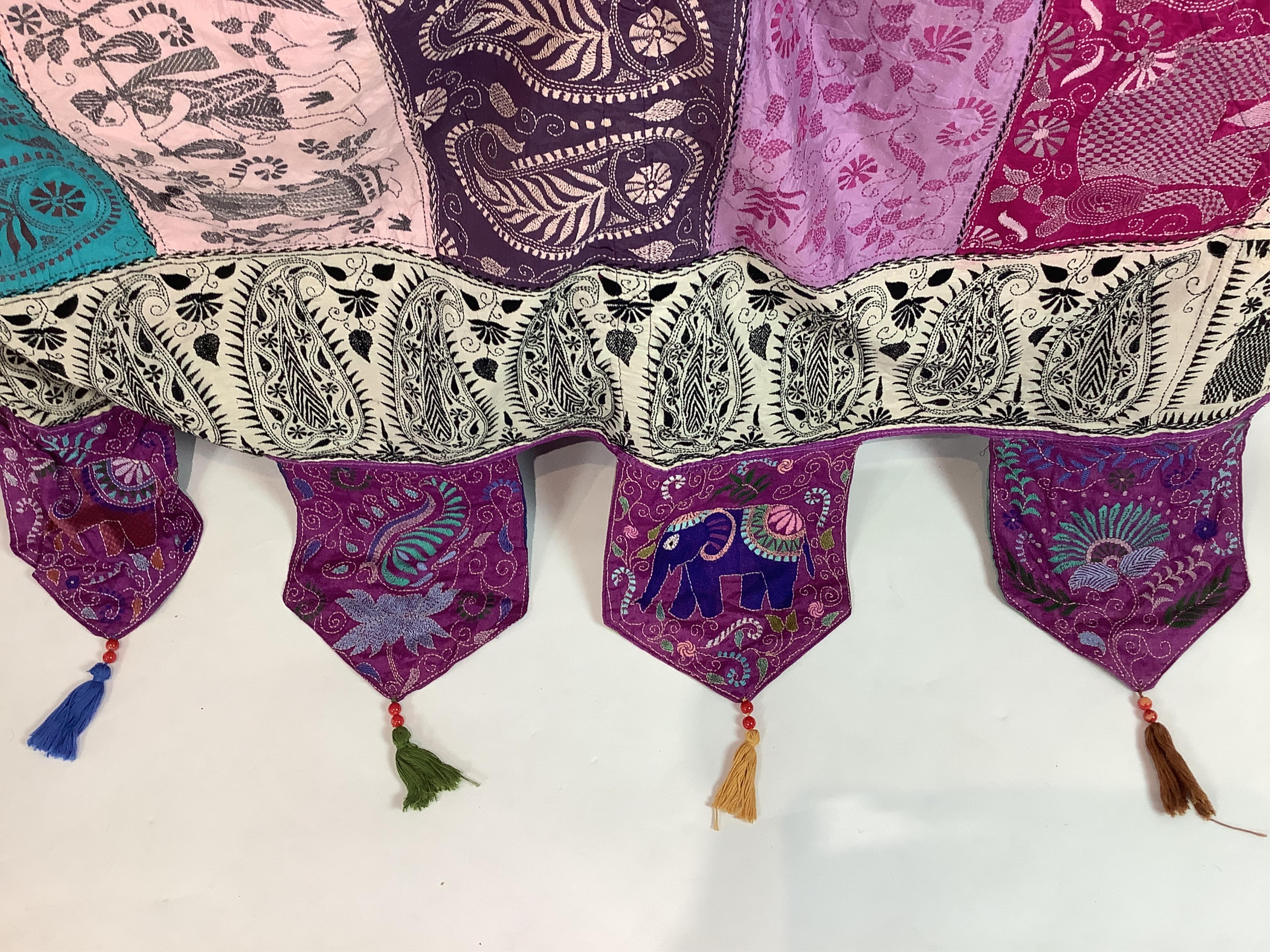 An Indian 20th century embroidered silk hanging, with decorative triangular tasselled edges. Worked in colourful silk stripes, with varying silk embroidered all over motifs. Bordered with colourful silk, beaded, tasselle